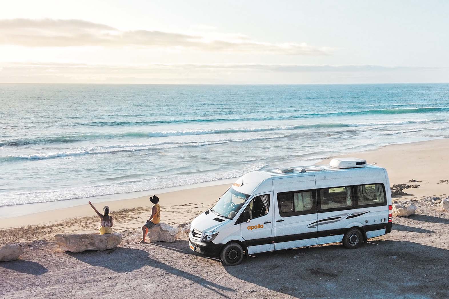 Couple sits next to Apollo Campervan at a South Australia beach